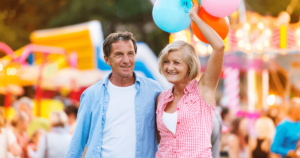 Older couple walking with balloons at Cottleville's local festival with rides behind them.